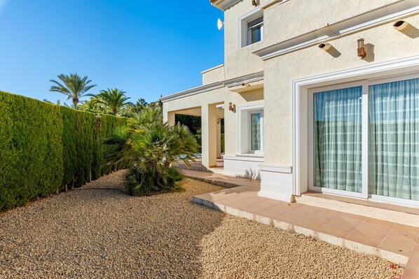 A modern two-story house with a well-maintained garden, a gravel driveway, and a clear blue sky.