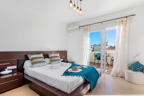 A modern bedroom with a large bed, bedside tables, a balcony with a table and chairs, and a view of the sky. - Villa Gran Sol 13 - PlusHolidays (Calpe)