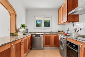 A modern kitchen with wooden cabinets, stainless steel appliances, and a window with a view of greenery.