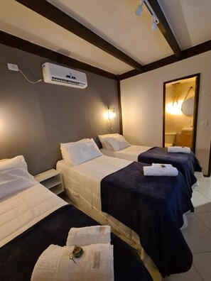 Une chambre d’hôtel avec deux lits, un ventilateur de plafond, un appareil de climatisation et une salle de bain visible à travers une porte ouverte.