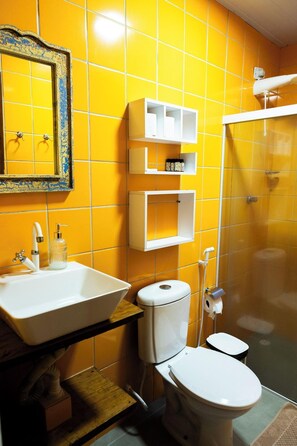 A bathroom with yellow tiles, a white sink, a toilet, and a shower. - Estrela Cordel (Fernando de Noronha)