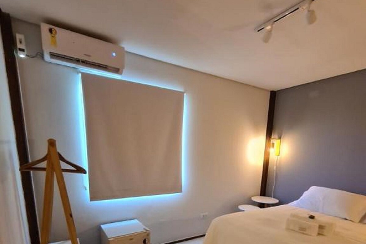 A hotel room with a bed, a wardrobe, a small table, an air conditioning unit, and a window with a view.