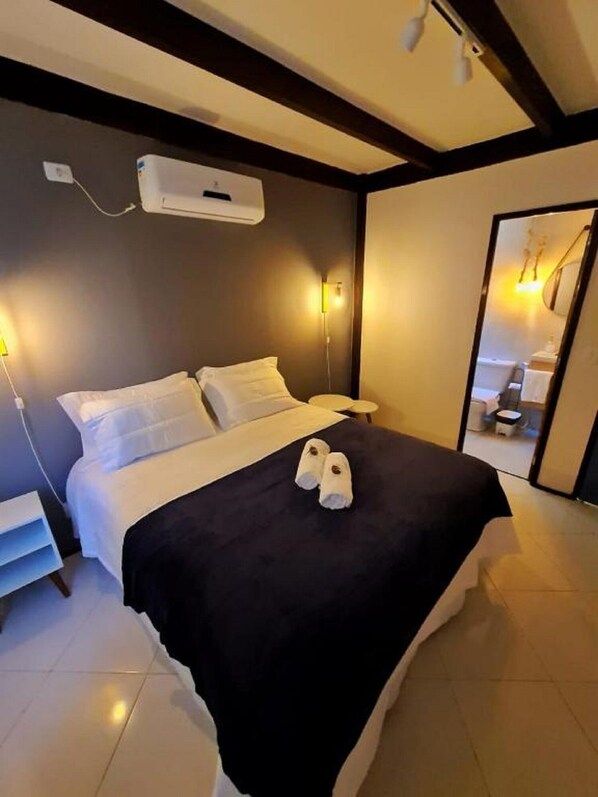 Une chambre d’hôtel comprenant un lit, des tables de chevet, un miroir et un climatiseur fixé au mur.