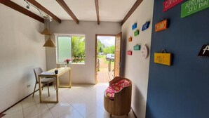 Una habitación con un escritorio, una silla y una pequeña mesa con un jarrón de flores. Hay carteles de colores en la pared y se ve el exterior.