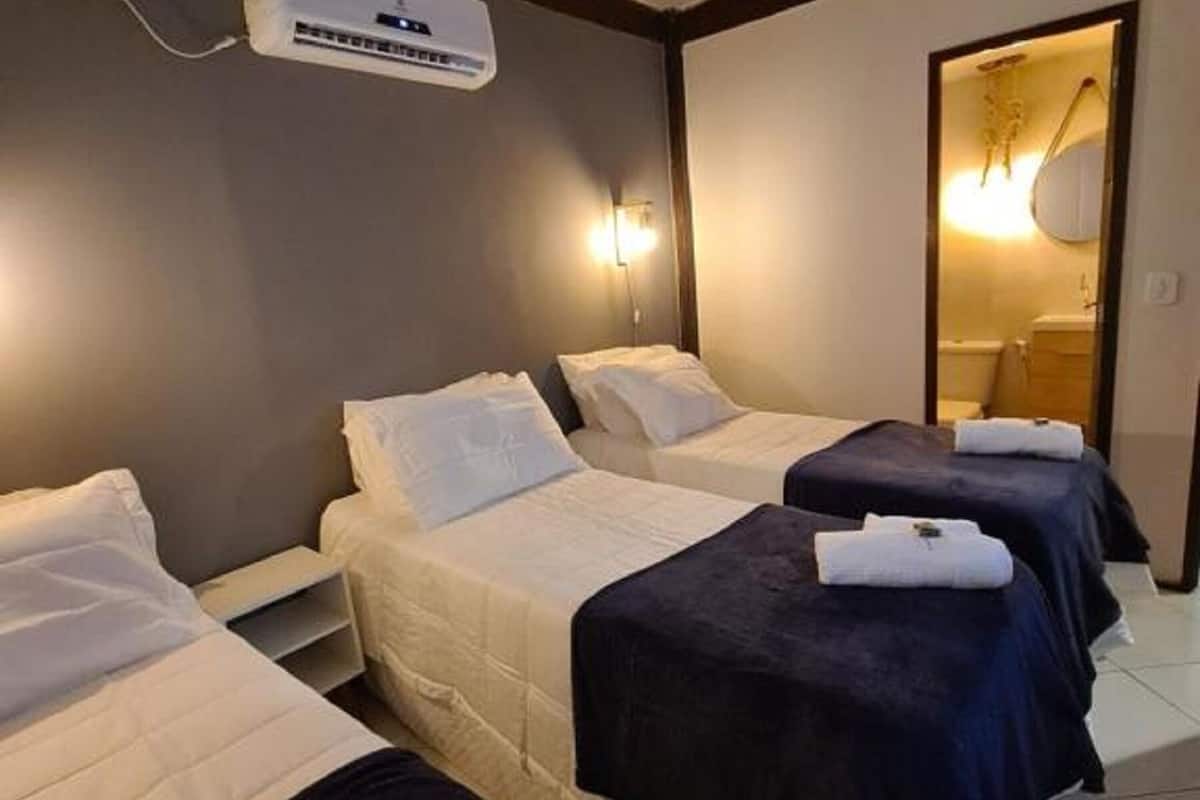 Ein Hotelzimmer mit drei Betten, einem Deckenventilator und einer Klimaanlage.