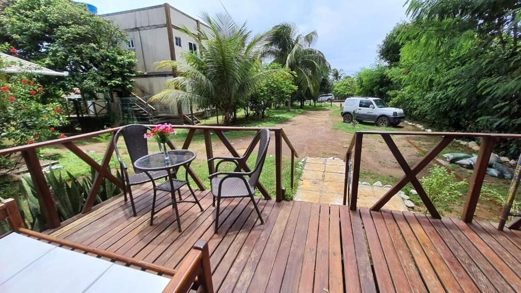 A wooden deck with two tables and chairs, surrounded by lush greenery and a pathway leading to a parked vehicle.