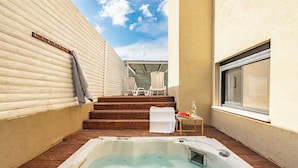 Zona de spa con un jacuzzi, escalones de madera, una mesita con una copa y una ventana.