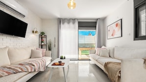 Una sala de estar moderna con un televisor de pantalla plana, dos sofás, una mesa de centro y un ventanal con vistas al exterior.