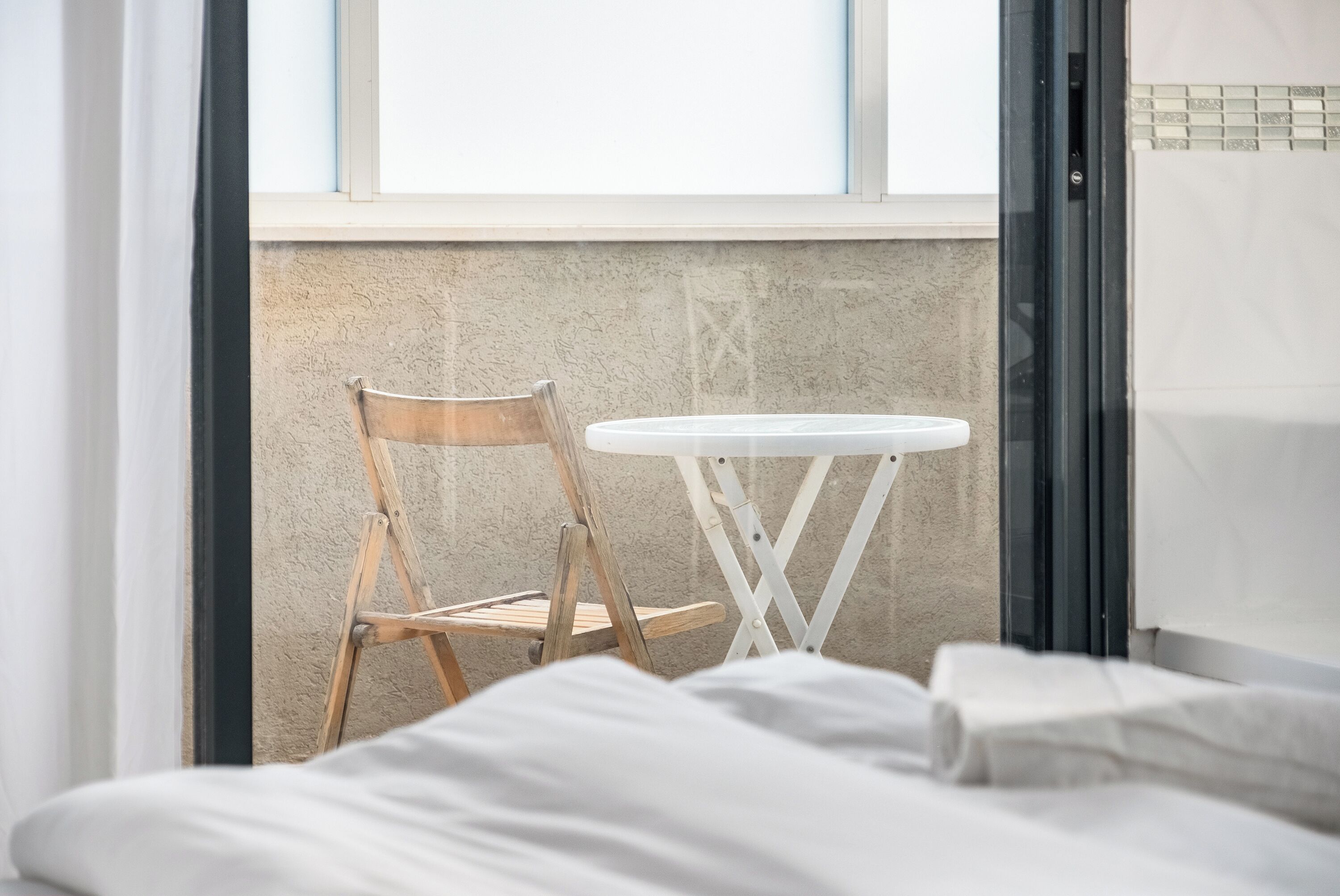 Una habitación con una cama, una silla de madera y una mesita blanca.