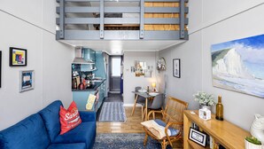 Un espacio habitable compacto con literas, kitchenette, comedor y un cuadro de una escena costera.