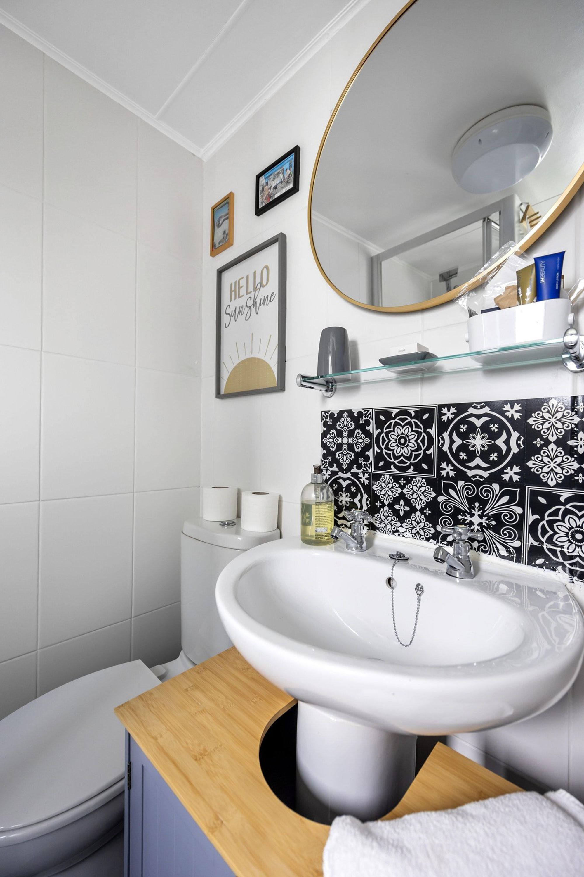 Un baño moderno con un lavabo blanco, un mueble de tocador de madera, un inodoro y un salpicadero de baldosas con diseño blanco y negro.