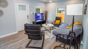 Un salon de taille modeste, doté d’un ventilateur de plafond, d’un téléviseur, d’un canapé, d’un fauteuil et d’une lampe.