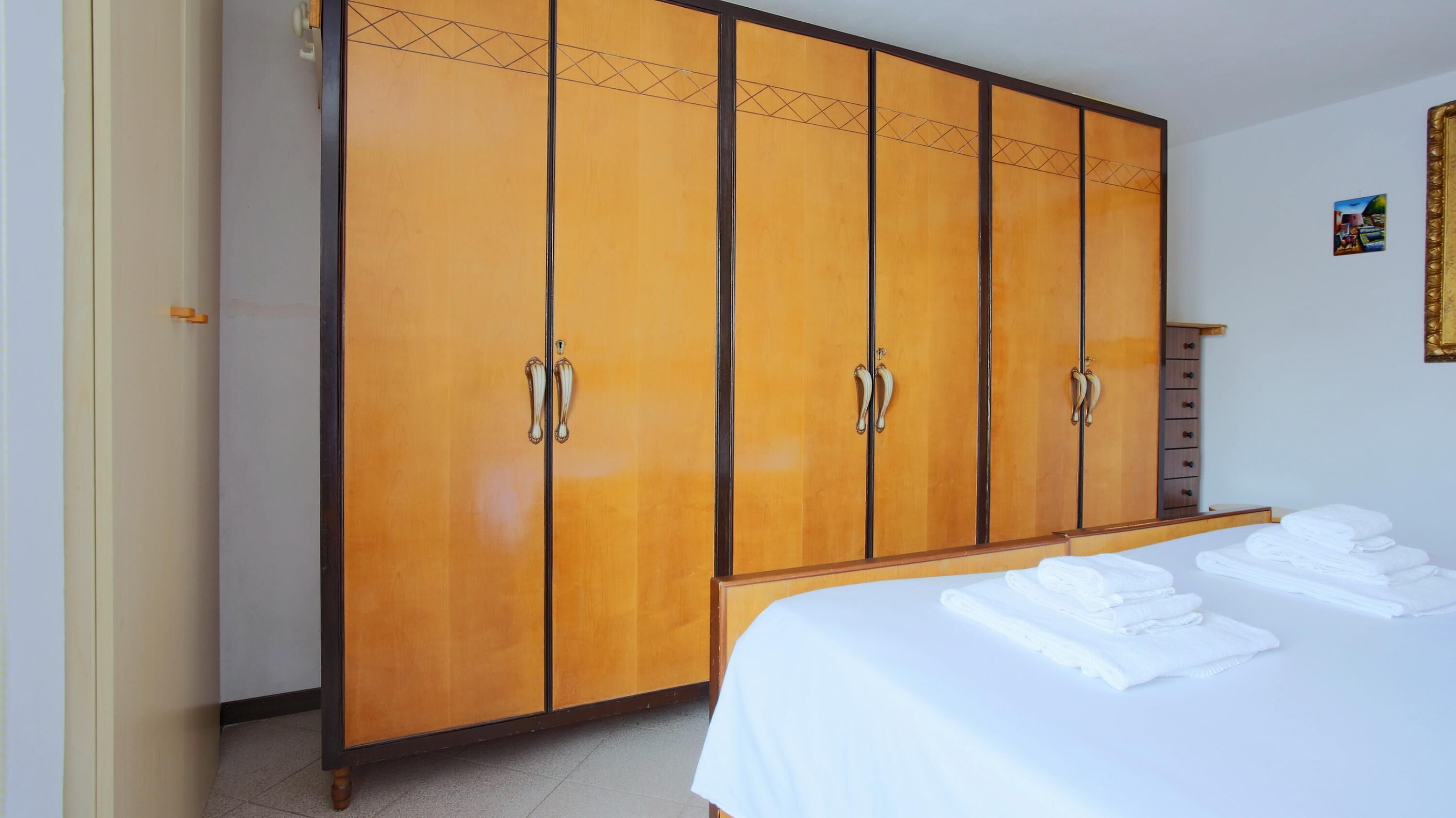 Una habitación de hotel con un armario grande de madera, una cama bien hecha y una cómoda pequeña de madera.