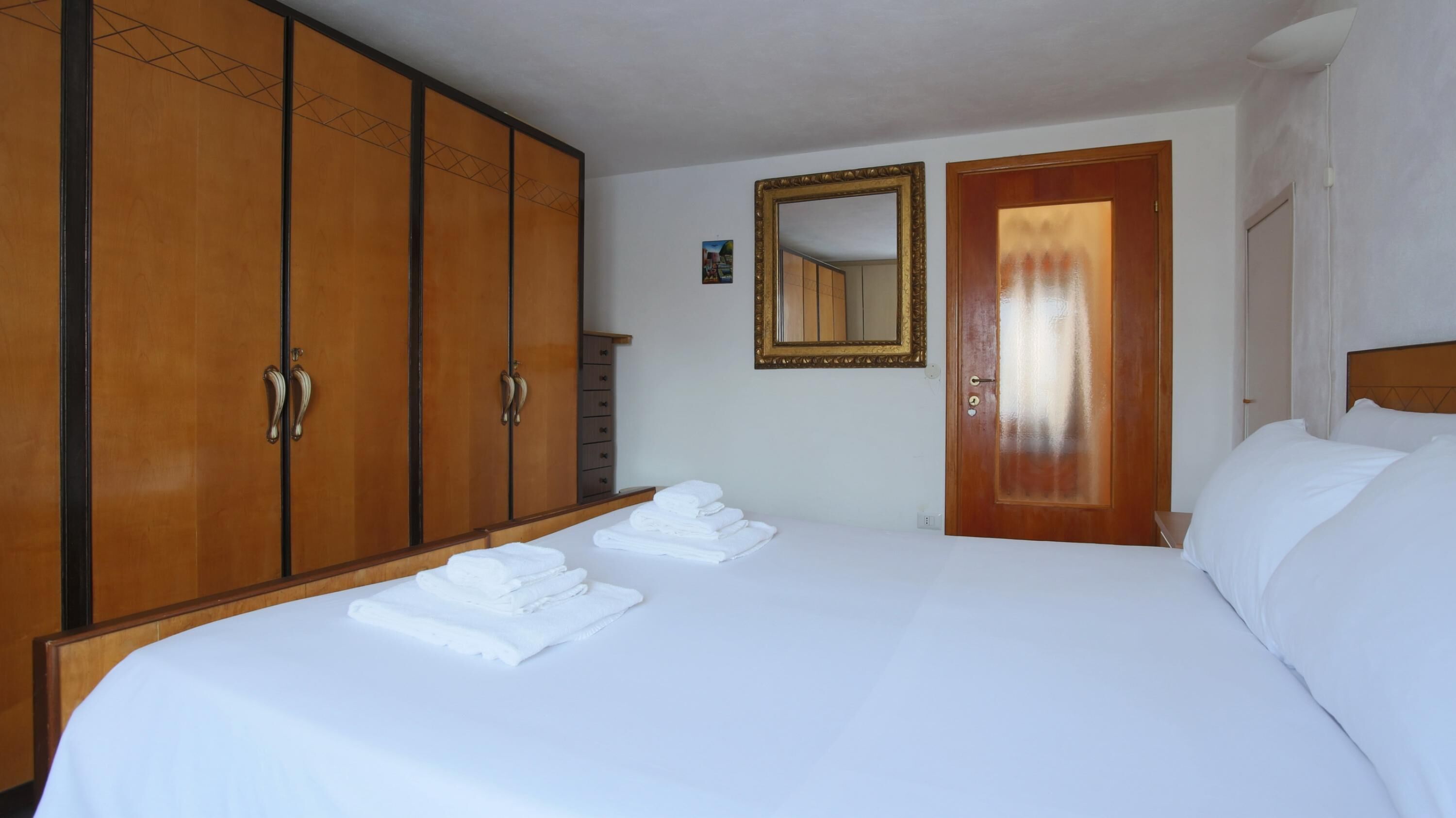 Una habitación de hotel con una cama grande, un armario, un espejo y una puerta.