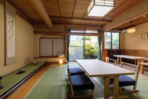 Une pièce de style japonais traditionnel, avec un sol recouvert de tatamis, une table basse entourée de bancs et une porte coulissante donnant sur un jardin.