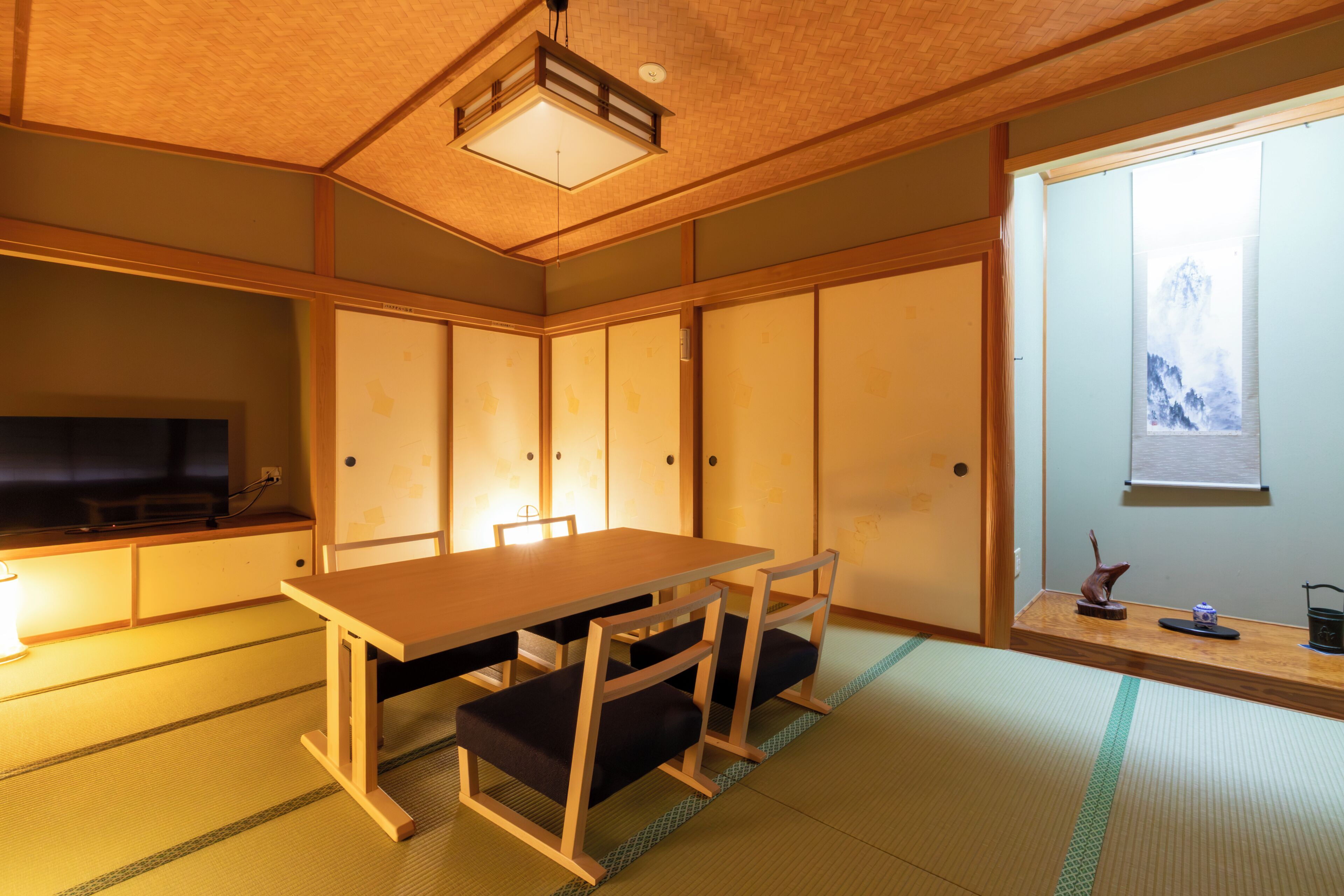 A traditional Japanese room with tatami flooring, a low table with cushions, sliding doors, and a television on the left.