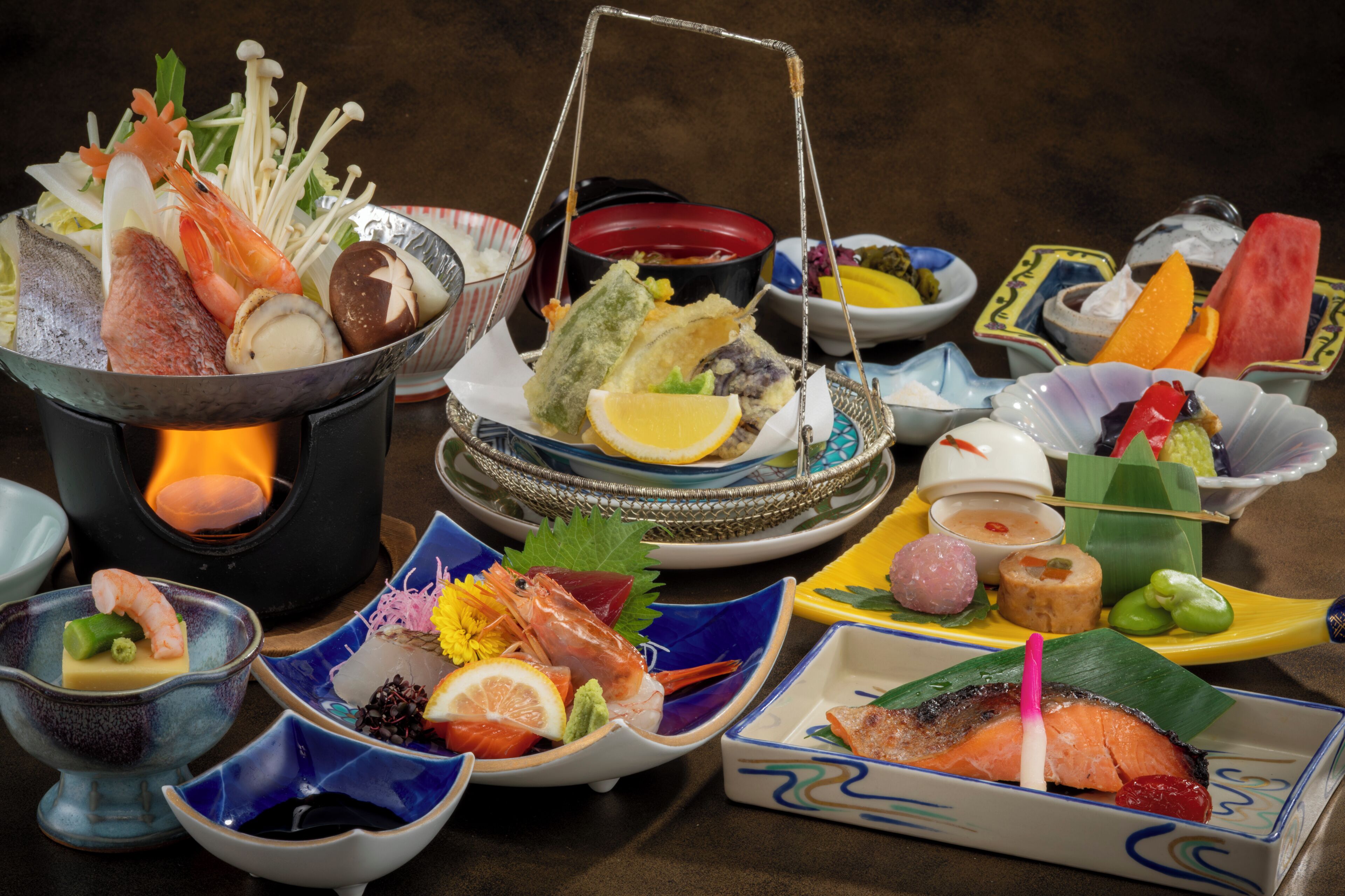 Variedad de platos japoneses, incluyendo sushi y sashimi, dispuestos sobre una mesa con una olla caliente en el centro.