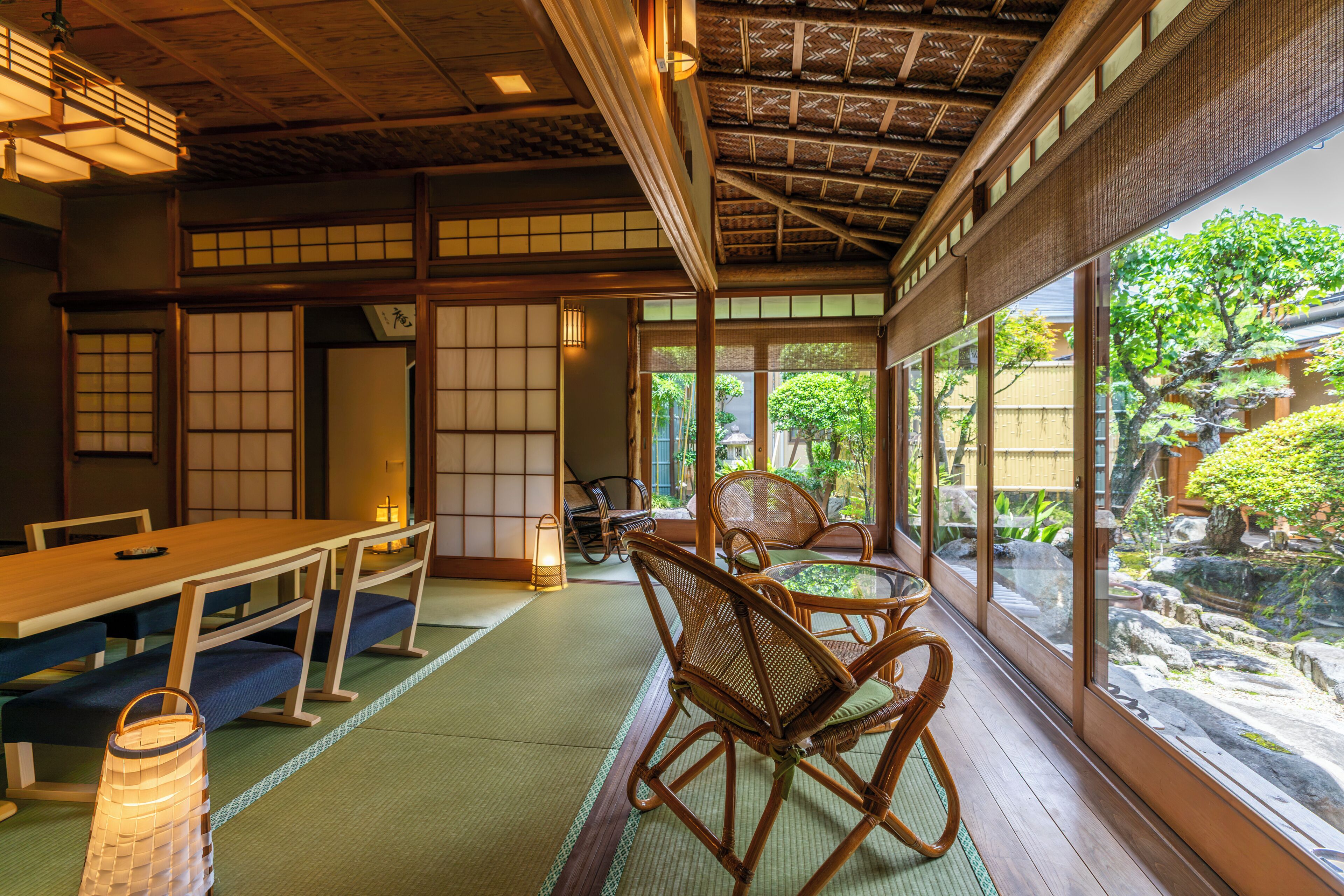 Ett traditionellt japanskt rum med tatamimattor på golvet, ett lågt bord och utsikt över en trädgård genom stora fönster.