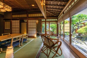 Una habitación japonesa tradicional con suelo de tatami, una mesa baja y vistas a un jardín a través de amplios ventanales.
