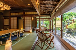 Una habitación japonesa tradicional con suelo de tatami, una mesa baja y vistas a un jardín a través de amplios ventanales.
