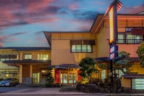 A traditional Japanese building with a modern entrance, a parking area, and a clear sky.