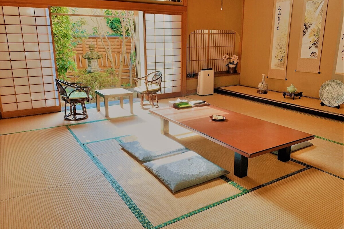 Um quarto japonês tradicional com tatames, uma mesa baixa e uma porta deslizante para um jardim.
