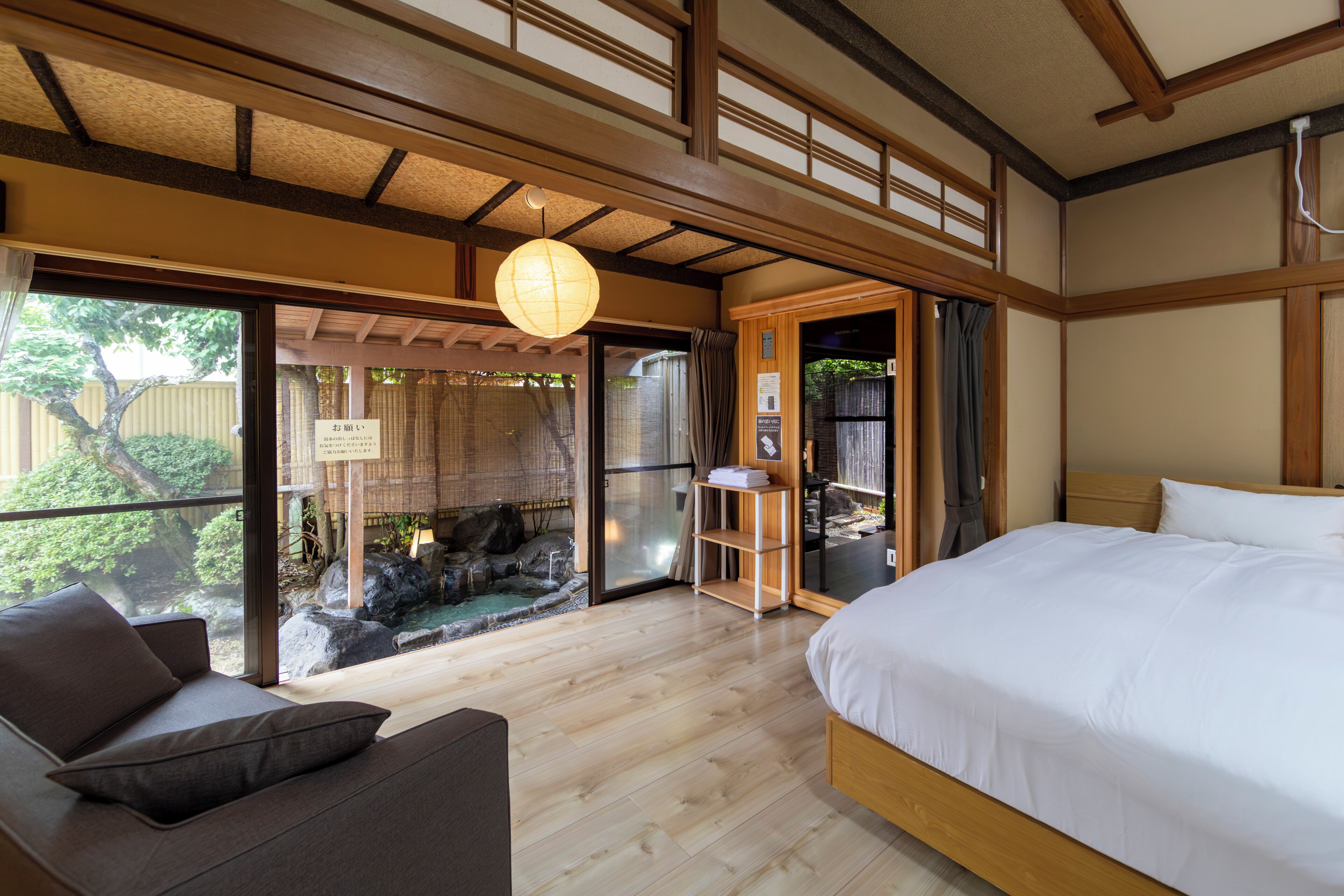 A traditional Japanese-style room with a bed, a wooden floor, and a view of a garden through a sliding door.