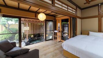 A traditional Japanese-style room with a bed, a wooden floor, and a view of a garden through a sliding door.