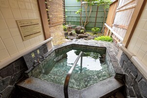 A stone hot spring with a wooden ladder, surrounded by tiled walls and a bamboo fence.
