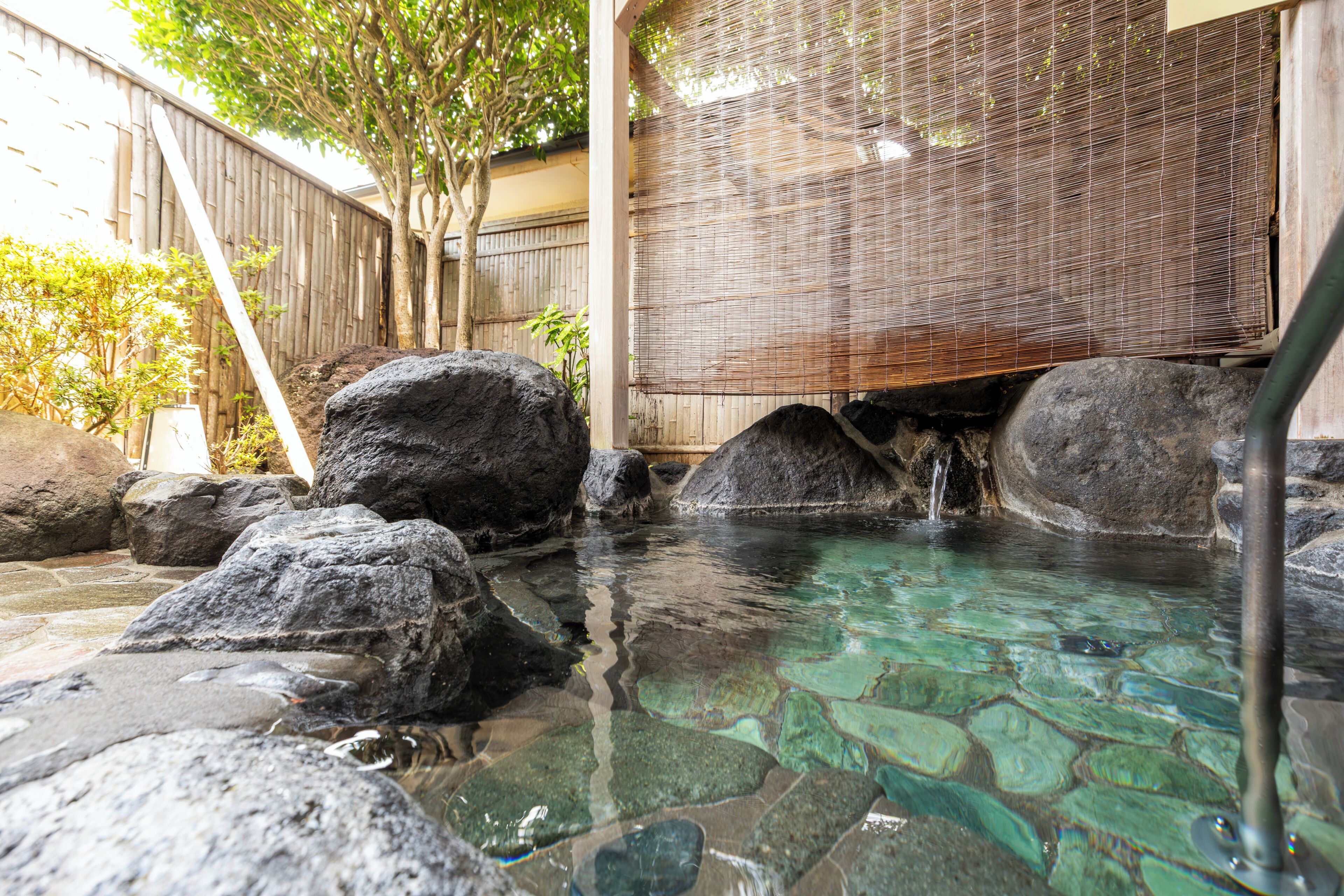 A hot spring area with clear water, large rocks, and a bamboo screen.