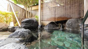 A hot spring area with clear water, large rocks, and a bamboo screen.