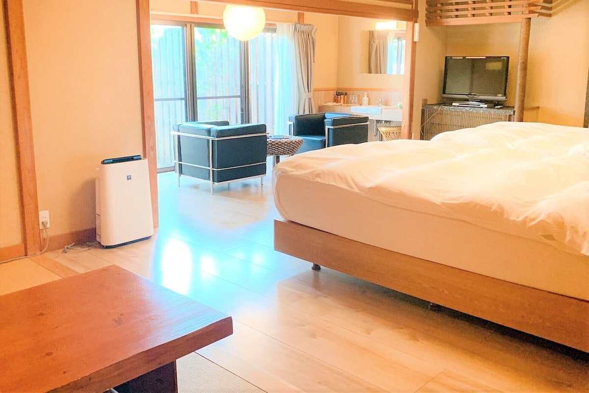 Quarto de hotel com uma cama grande, uma escrivaninha, uma cadeira, uma televisão e uma pequena cozinha.