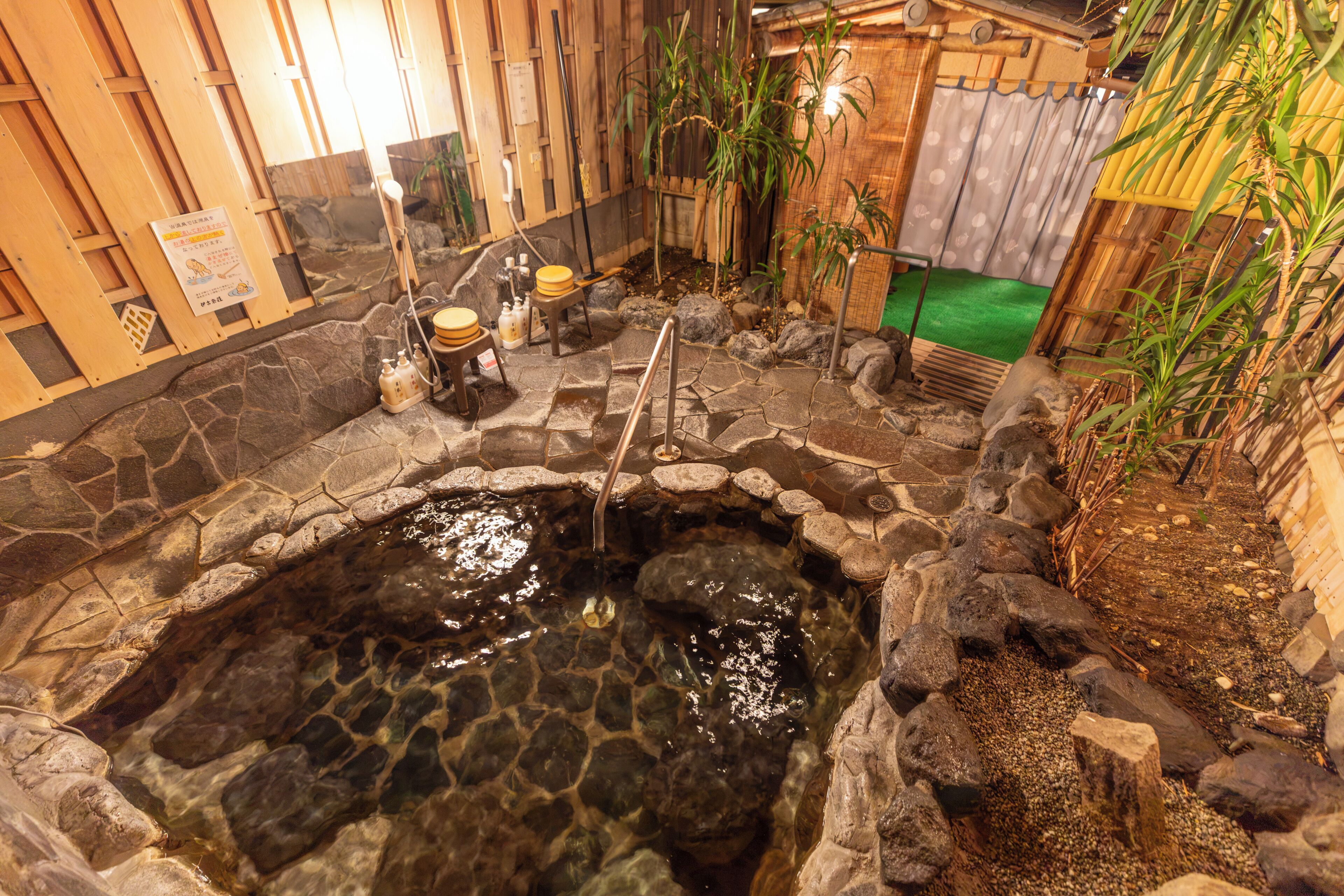 A hot spring bath area with stone walls, wooden benches, and a small waterfall feature.