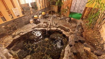 A hot spring bath area with stone walls, wooden benches, and a small waterfall feature.