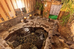 Un área de baños termales con paredes de piedra, bancos de madera y una pequeña cascada.