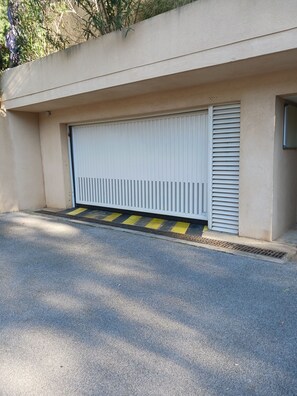 Een garage met een gesloten witte deur, een gele strook voelbare bestrating en een betonnen muur.