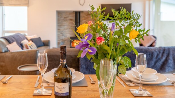 Una mesa de comedor dispuesta con una botella de Prosecco, dos copas y un florero con flores.