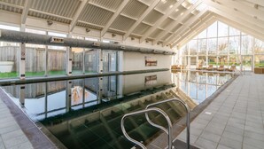 Una piscina interior con barrera de vidrio, escalera metálica y vistas al exterior a través de amplios ventanales.