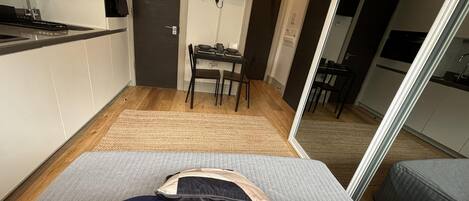 A compact living space with a kitchenette, a dining area, and a bed with a blue pillow.