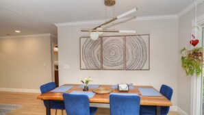 Zona pranzo con tavolo in legno, sedie blu e lampadario moderno al soffitto.