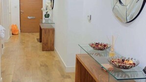 A hallway with wooden flooring, a bench, a glass table with a bowl of fruit, and a door at the end.