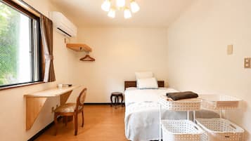Een kleine hotelkamer met een bed, een bureau, een stoel, een kapstok en wasmanden.