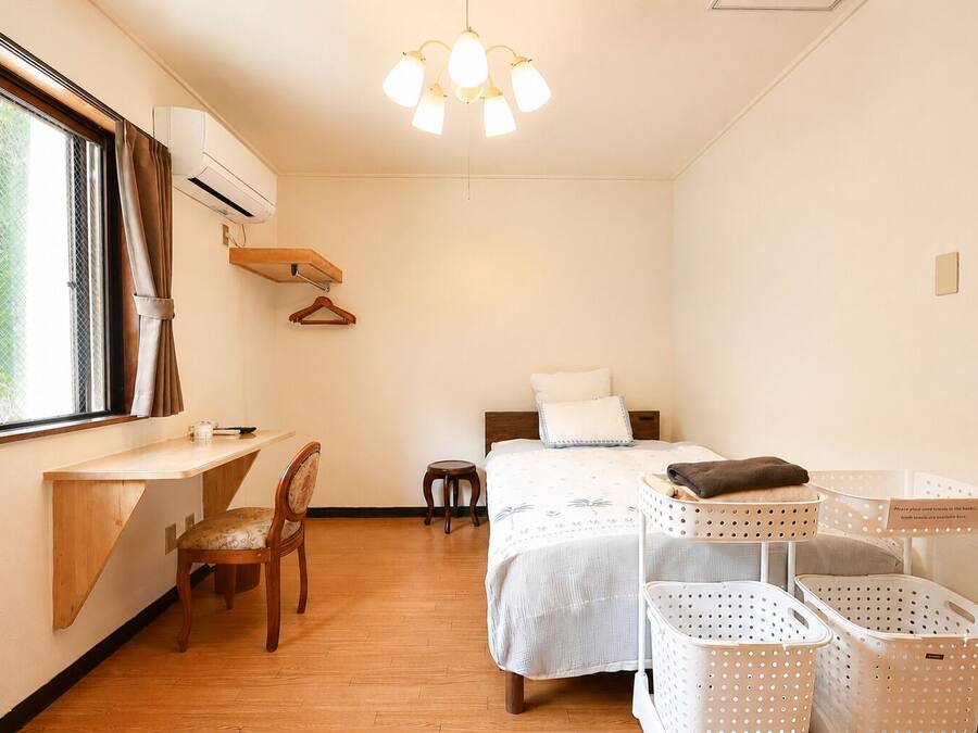 Een kleine hotelkamer met een bed, een bureau, een stoel, een kapstok en wasmanden.