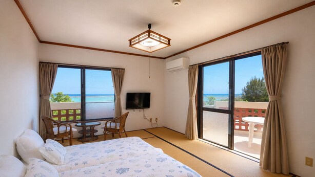 A hotel room with a bed, a TV, a balcony with a table and chairs, and a view of the sea. - Beach side Pension mibal (Nanjo)