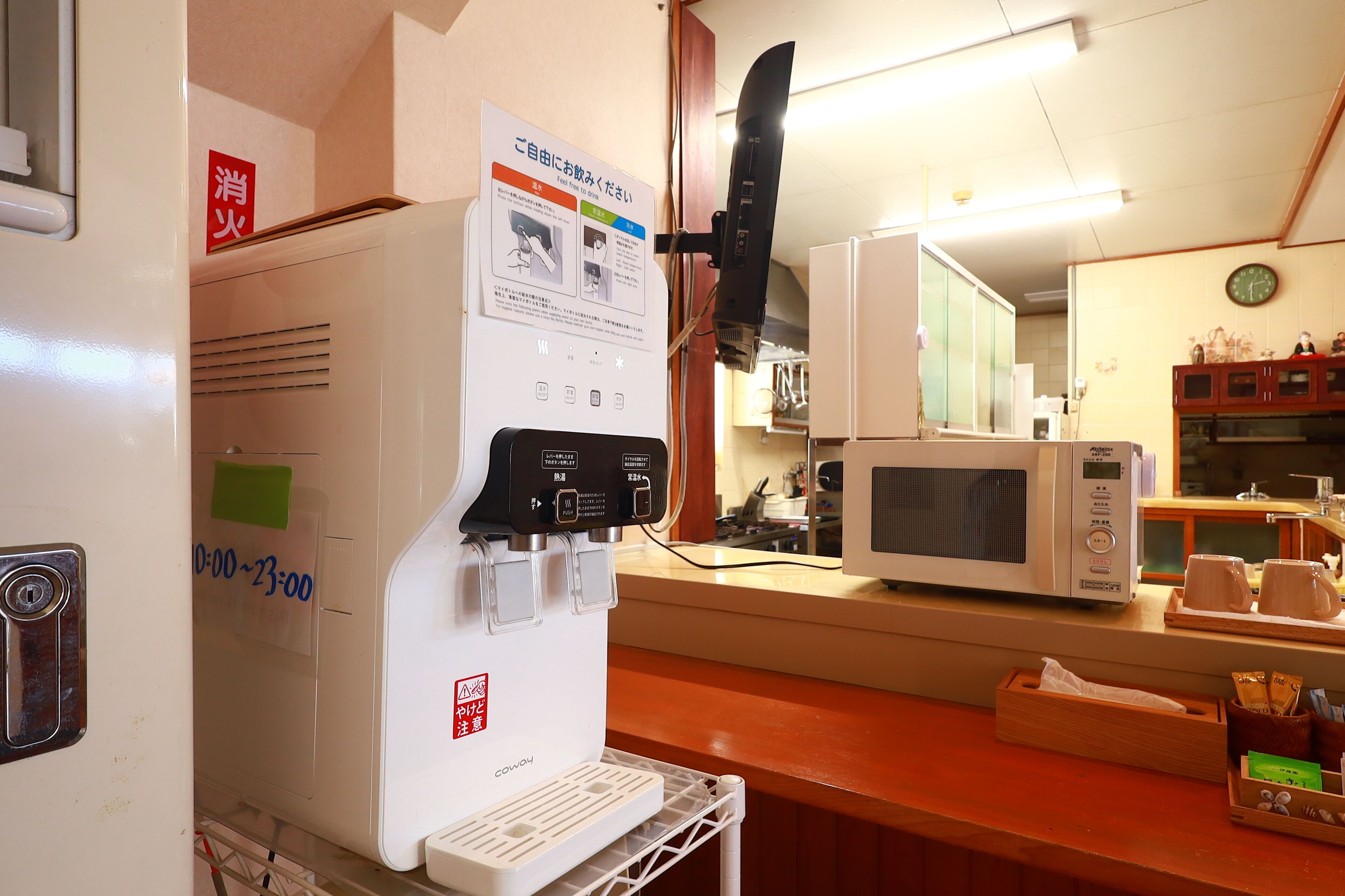 A kitchen area with a water dispenser, microwave, and a clock on the wall.
