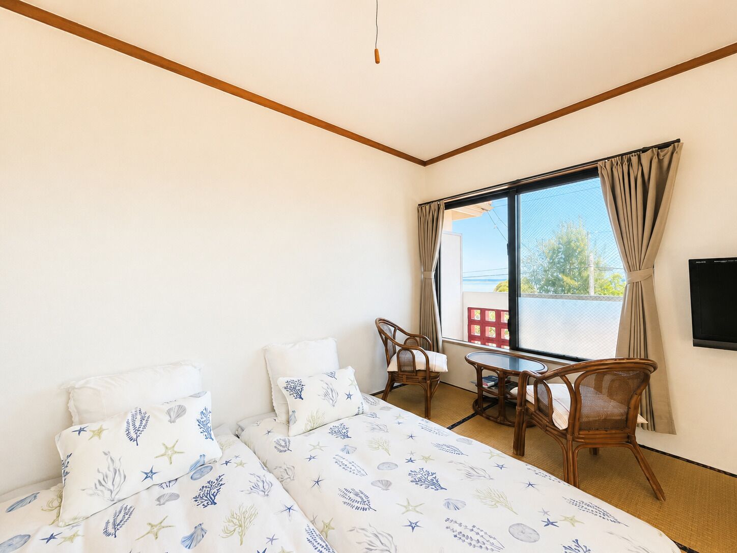A hotel room with a bed, two chairs, a small table, and a TV on the wall.