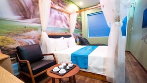 A hotel room with a bed, a chair, a small table with tea sets, and a mural of a waterfall. - Huong Duong Hotel Yen Xa by Bay Luxury (Hanoi)