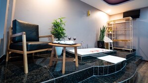 A modern bathroom with a black marble floor, a wooden chair, a small table with a plant, and a shelf with towels. - Huong Duong Hotel Yen Xa by Bay Luxury (Hanoi)