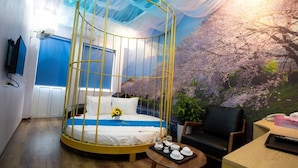 A room with a bed in a yellow canopy, a desk with a chair, a small table, and a wall mural of cherry blossoms. - Huong Duong Hotel Yen Xa by Bay Luxury (Hanoi)