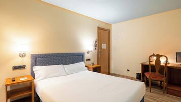 Una habitación de hotel con cama, mesitas de noche, escritorio y silla.